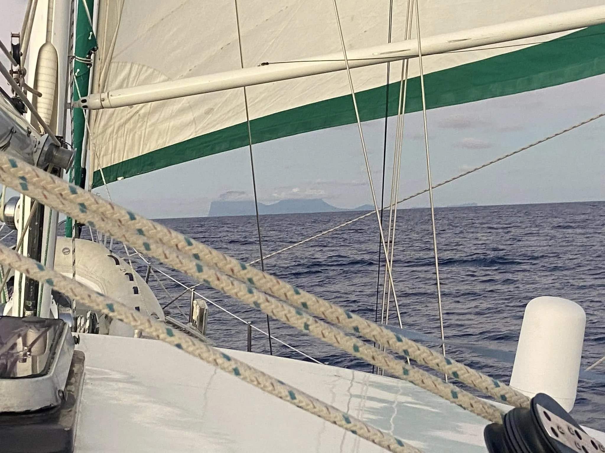 Sea Dragon's white sails with green trim, the coastline on the horizon