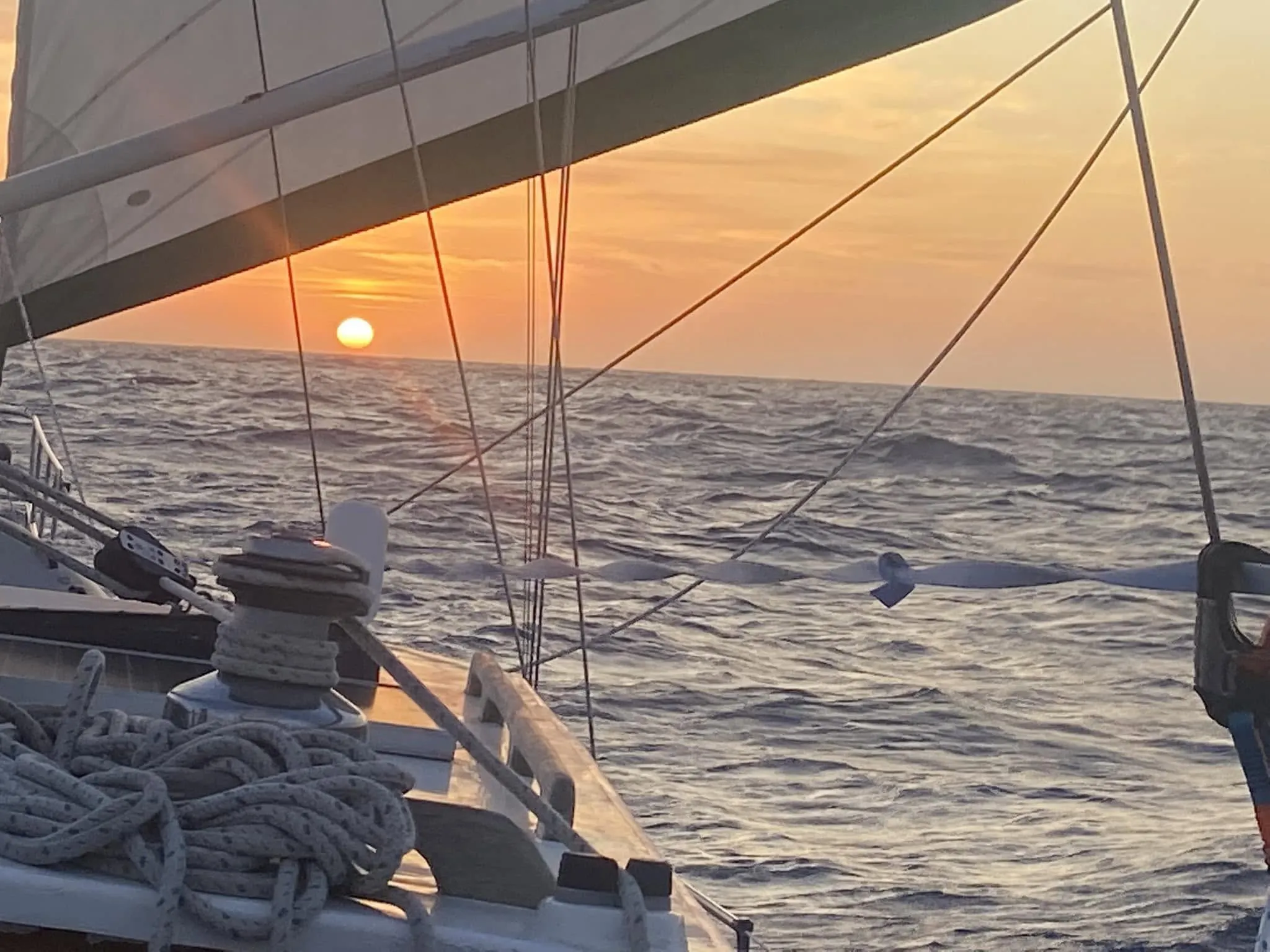 The sun setting over the ocean seen past Sea Dragon's winch and sheets