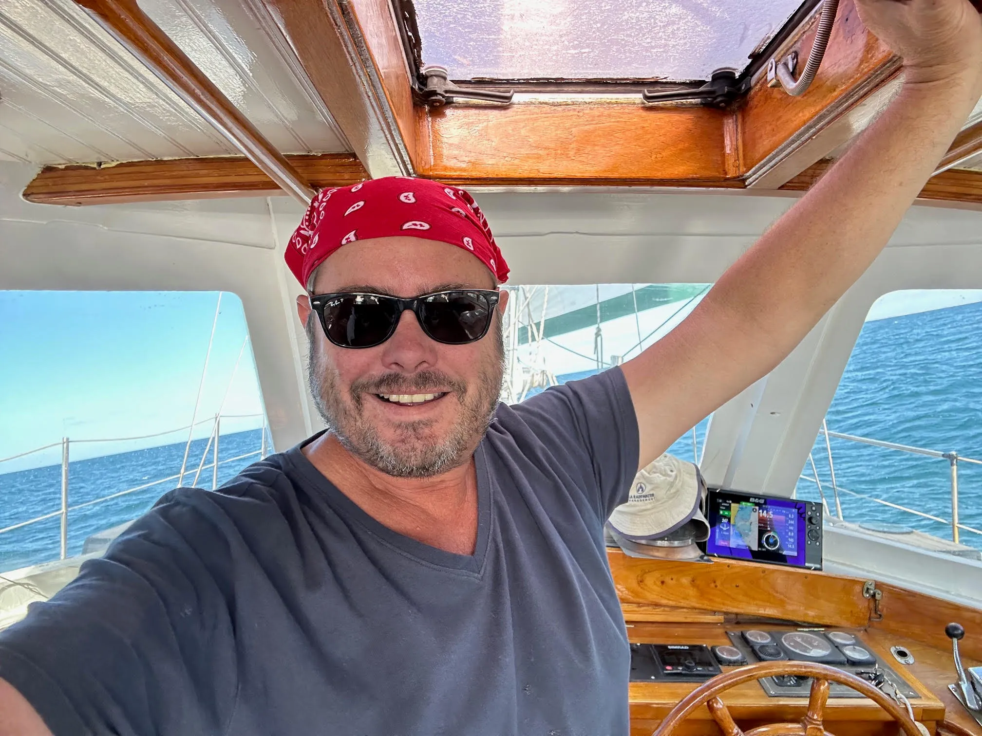 Tim at Sea Dragon's helm in a red bandana and sunglasses, the sea behind him
