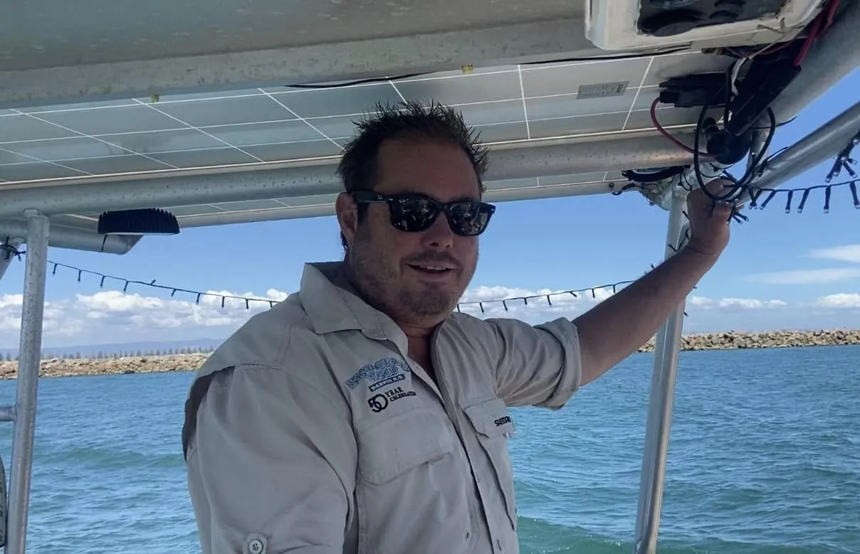 Tim Whitrow smiling at Sea Dragon's helm under the bimini